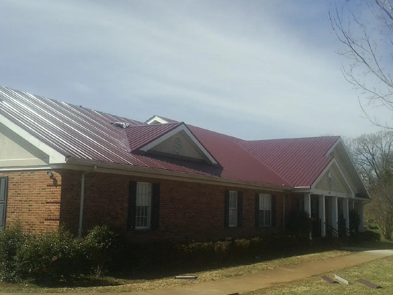 Red metal roof with gabled entries on a long brick building, from a Hail Damage Roof Repair job in Dinwiddie