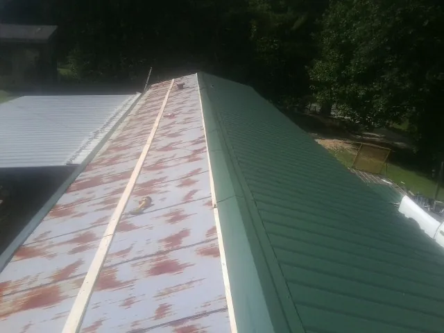 Old rusted panels beside newly installed green metal roofing — Wind Damage Roof Repair by Roofing Brothers in Dinwiddie