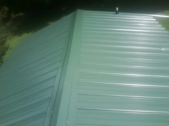 New green metal panels meeting at the ridge of a roof — Flat Roof Repair work by our crew in Dinwiddie