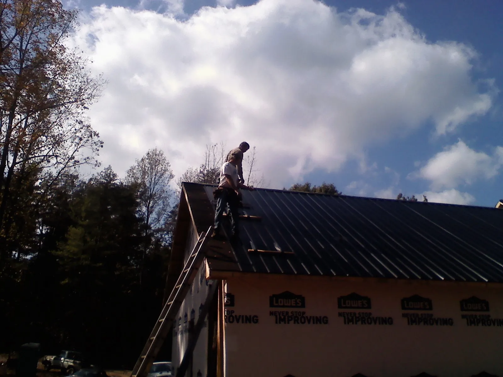 Roofer fastening dark metal panels high against a cloudy sky, from a Roof Inspection job in Dinwiddie