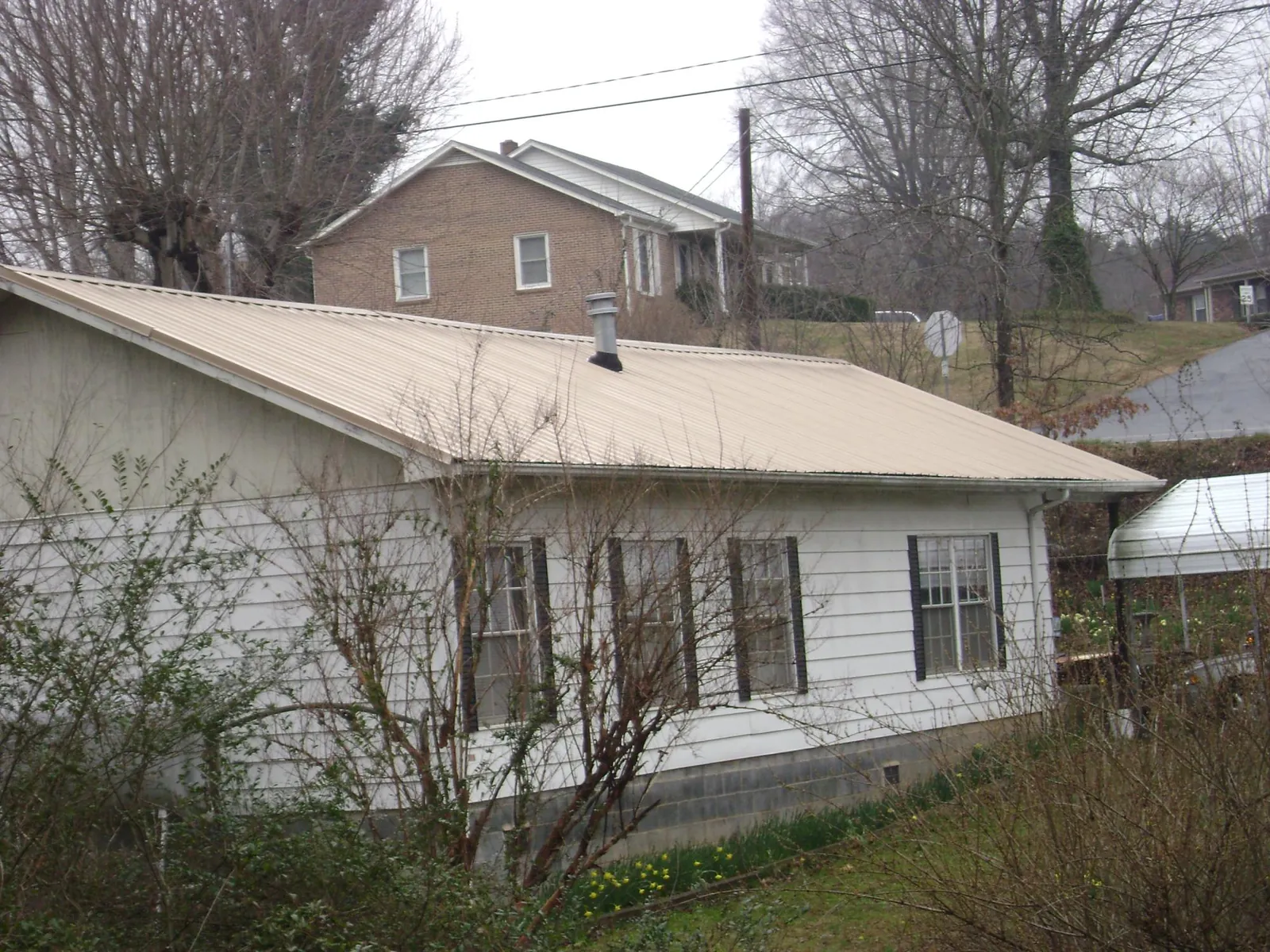 Tan metal roof on a white sided house set into a hillside — Commercial Roofing by Roofing Brothers in Dinwiddie